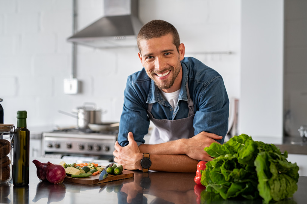 modern man smiling in the kitchen with sliced up food in the countertop
