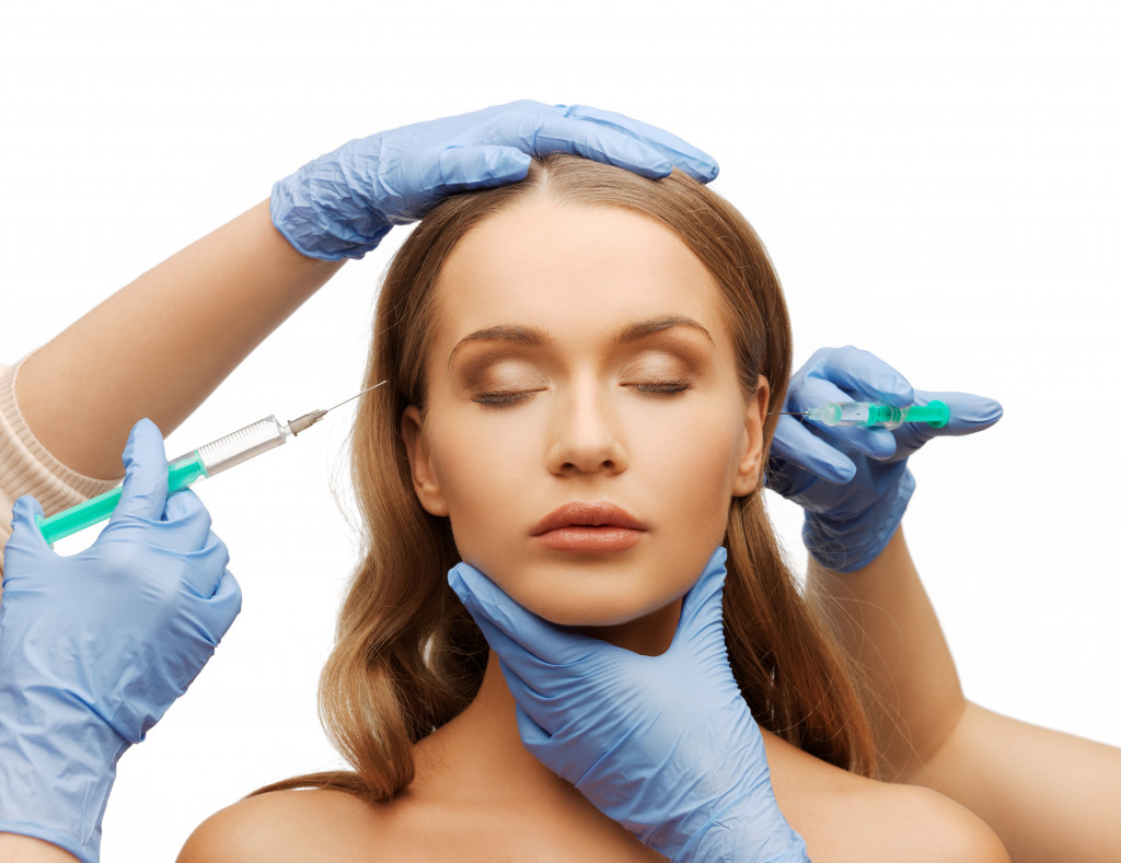 woman face and beautician hands with syringes